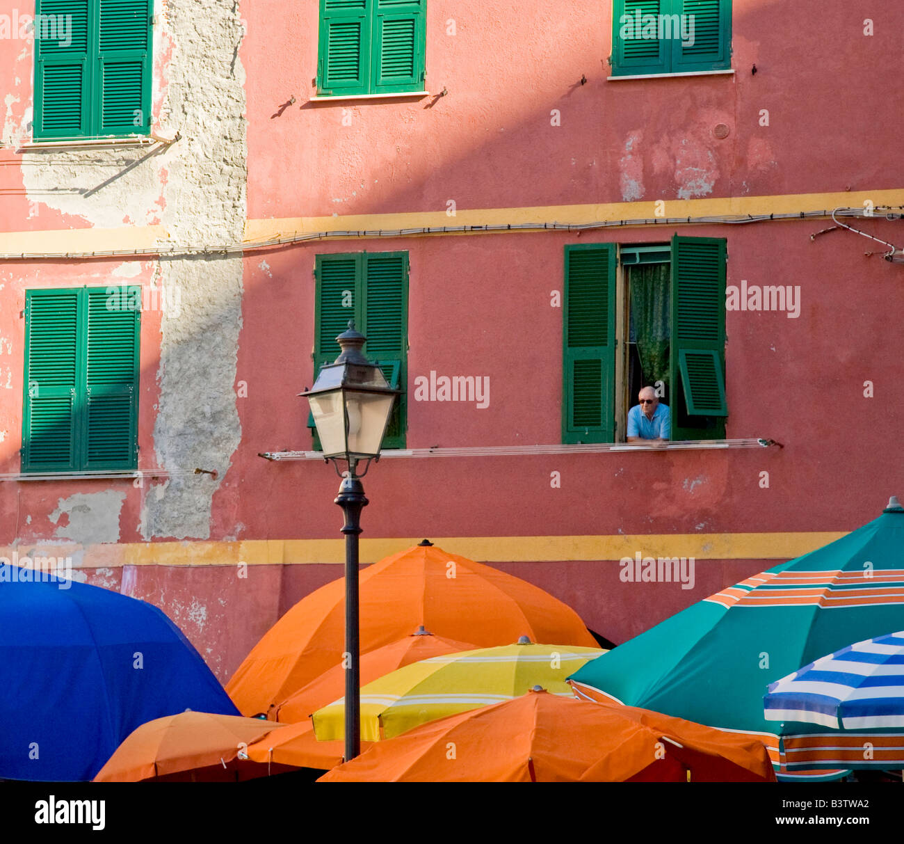 L'Europe, l'Italie, les Cinque Terre, Vernazza. L'homme de la fenêtre aux volets verts pairs parasols colorés ci-dessus. Banque D'Images
