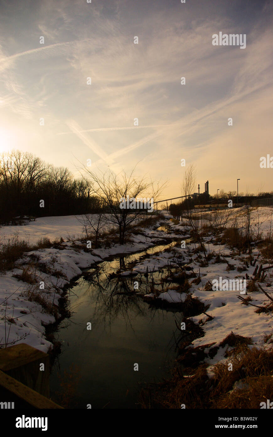 Le soleil se couche sur un paysage enneigé avec un flux qui partent vers une centrale à charbon. Banque D'Images