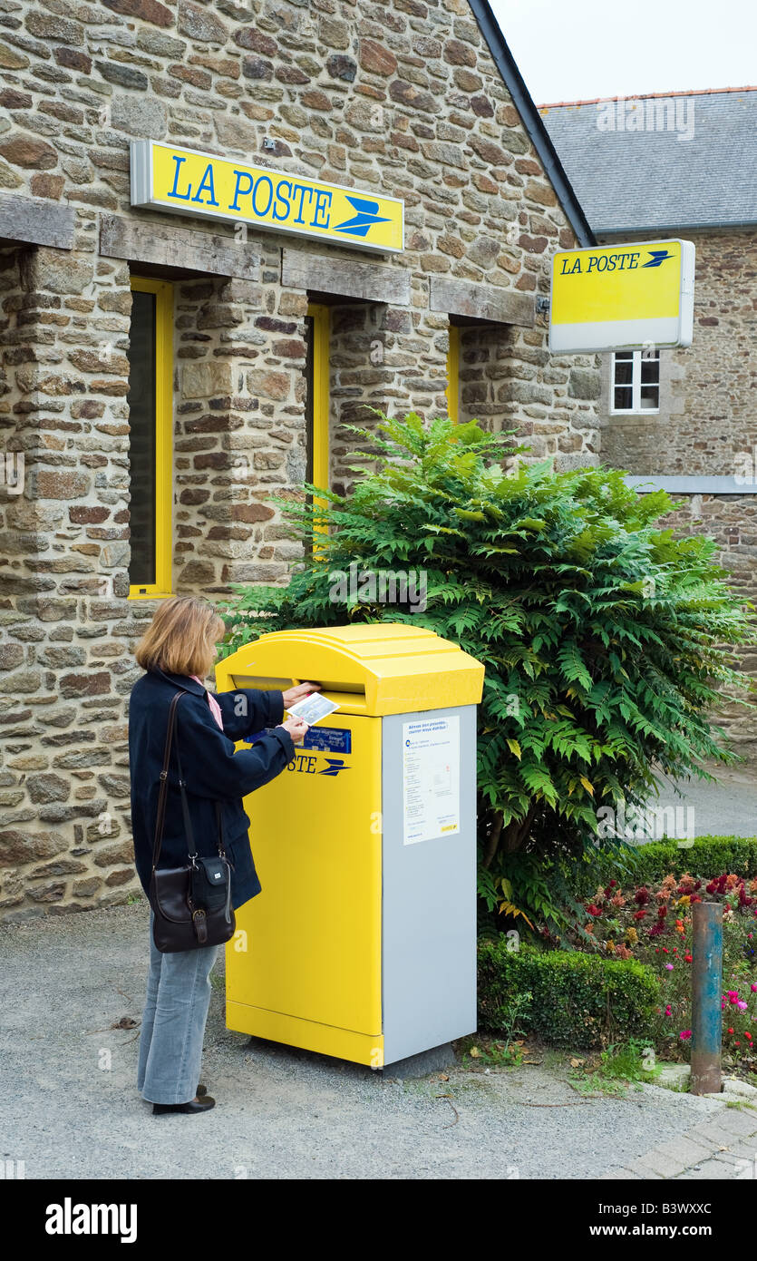 Femme postant du courrier dans la boîte aux lettres pilier devant le bureau de poste, la poste, Plancoët village Bretagne France Europe Banque D'Images