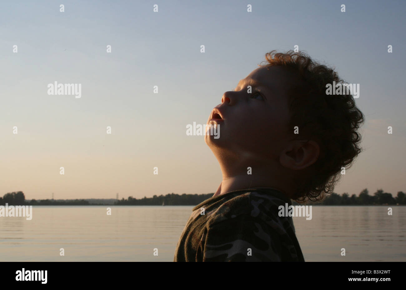 Un jeune garçon au bord du lac, qui est à regarder un avion dans le ciel. Banque D'Images