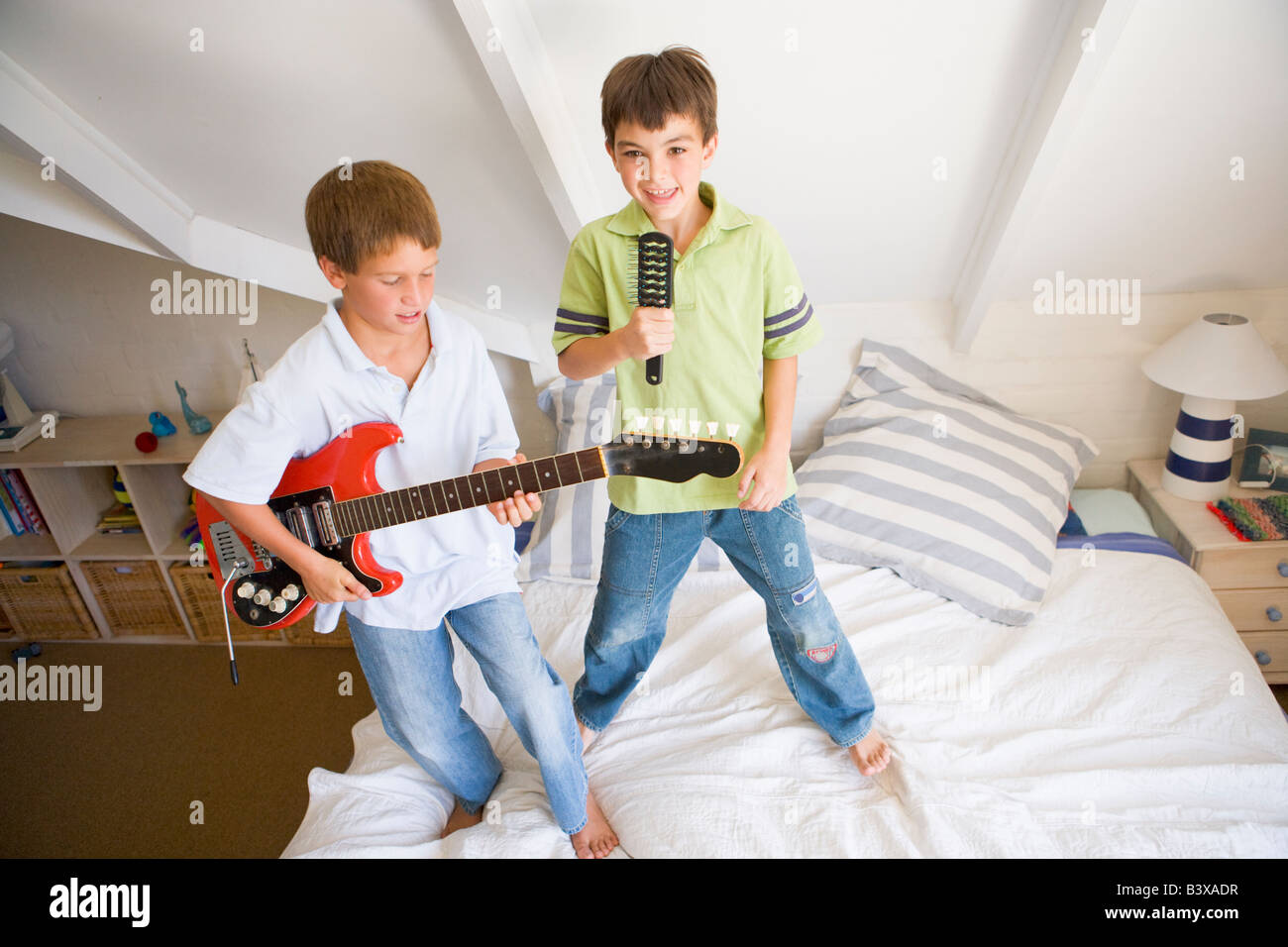 Deux garçons debout sur un lit, à jouer de la guitare et chanter dans une brosse Banque D'Images