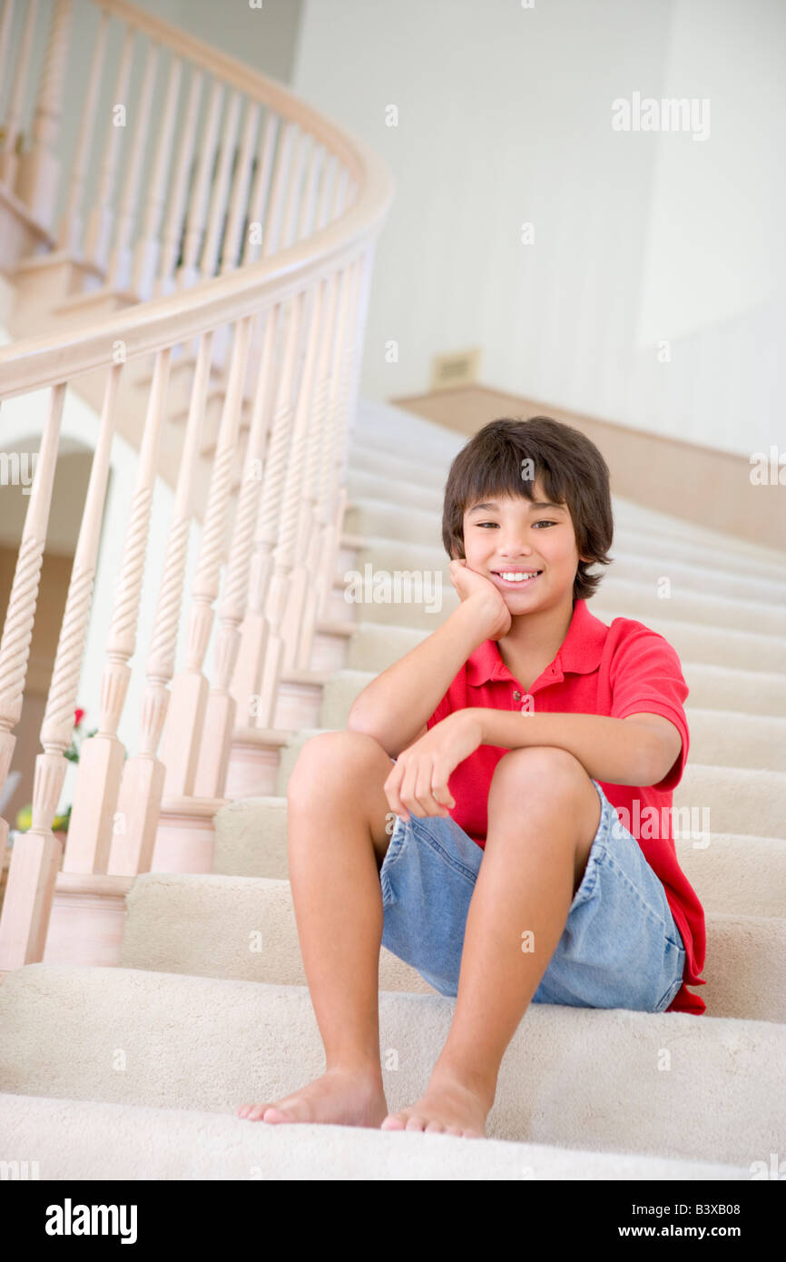 Jeune garçon assis sur un escalier à la maison Banque D'Images