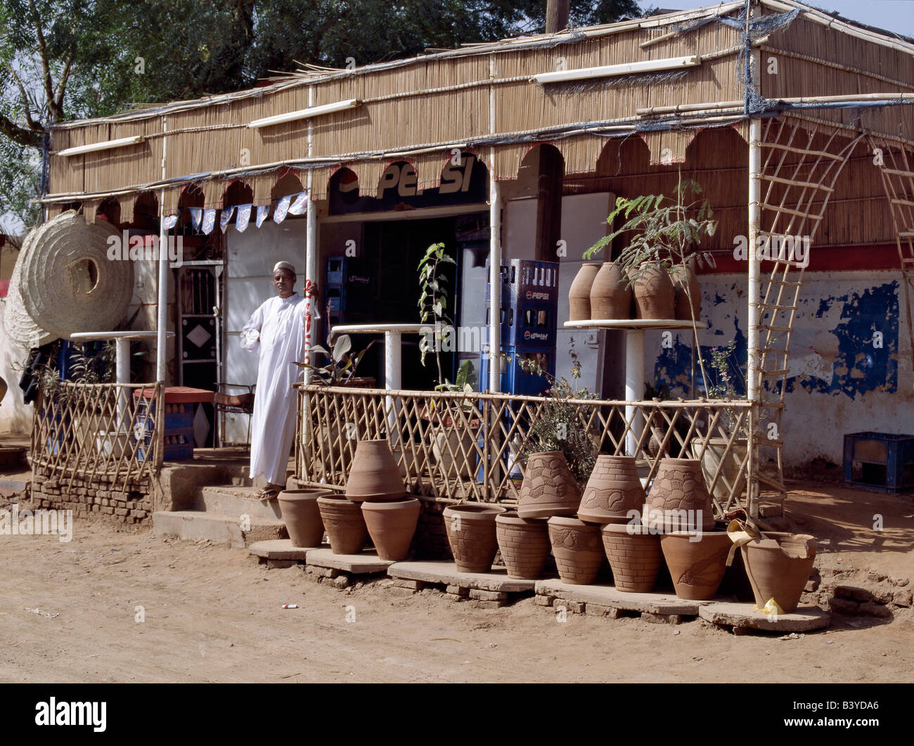 Soudan, Khartoum, Omdurman. Le propriétaire d'une boutique de la route attend les clients sur sa terrasse à côté de la marchandise soigneusement aménagées. Banque D'Images