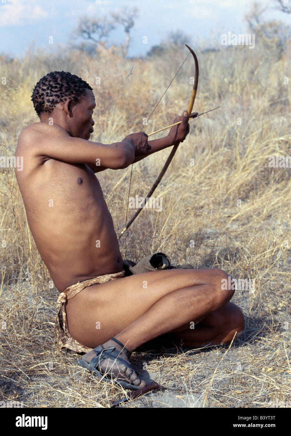 La Namibie, l'Est Bushmanland, Tsumkwe. Un chasseur-cueilleur !Kung vérifie sa corde de l'arc, qu'il a faite à partir de la nature des fibres sis Banque D'Images
