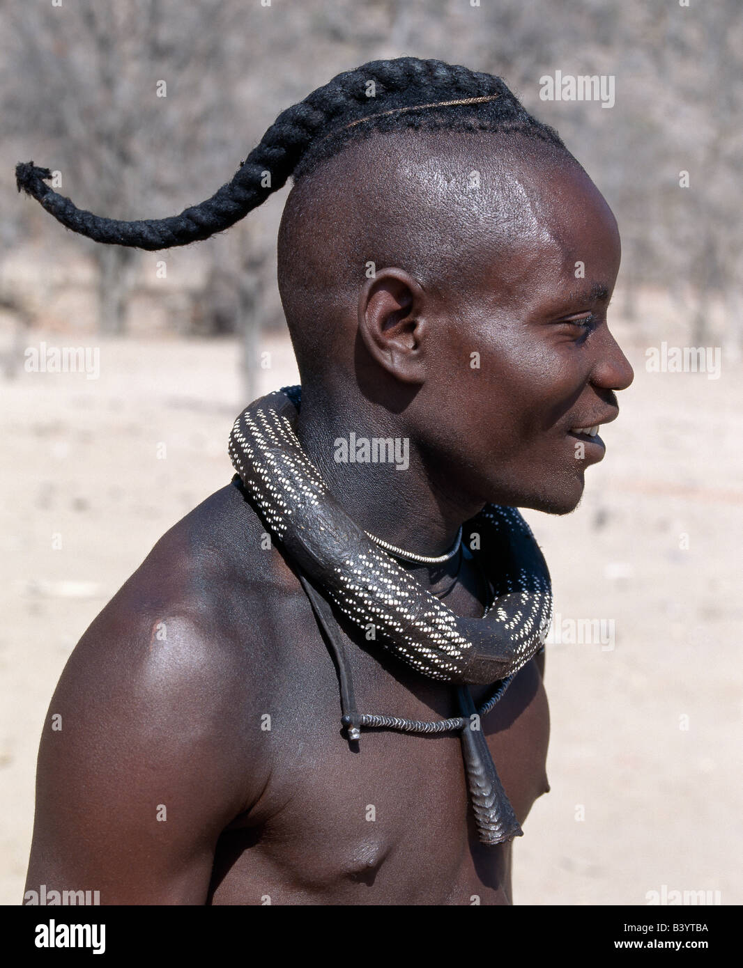 La Namibie, Kaokoland, Epupa. Un jeune Himba a son style de cheveux en une longue natte, connu comme ondatu. Une fois marié, il va diviser le ondatu en deux tresses et les garder couverts. Son blanc-beaded necklace, ombwari, auront été faites pour lui par sa mère. Suspendu à ses petits collier est une corne d'antilope.Les Himbas Herero Bantu francophone sont des nomades qui vivent dans les conditions difficiles, sec mais très beau paysage de la nord-ouest de la Namibie. Banque D'Images