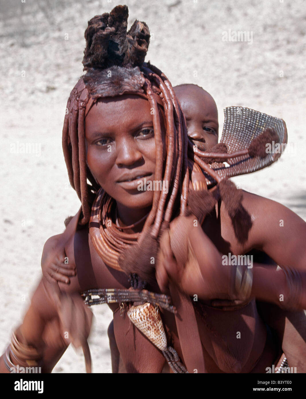 La Namibie, Kaokoland, Empembe. Une mère Himba se déplace pour avoir son bébé à l'aise dans un porte-bébé en cuir sur son dos. Leur Banque D'Images