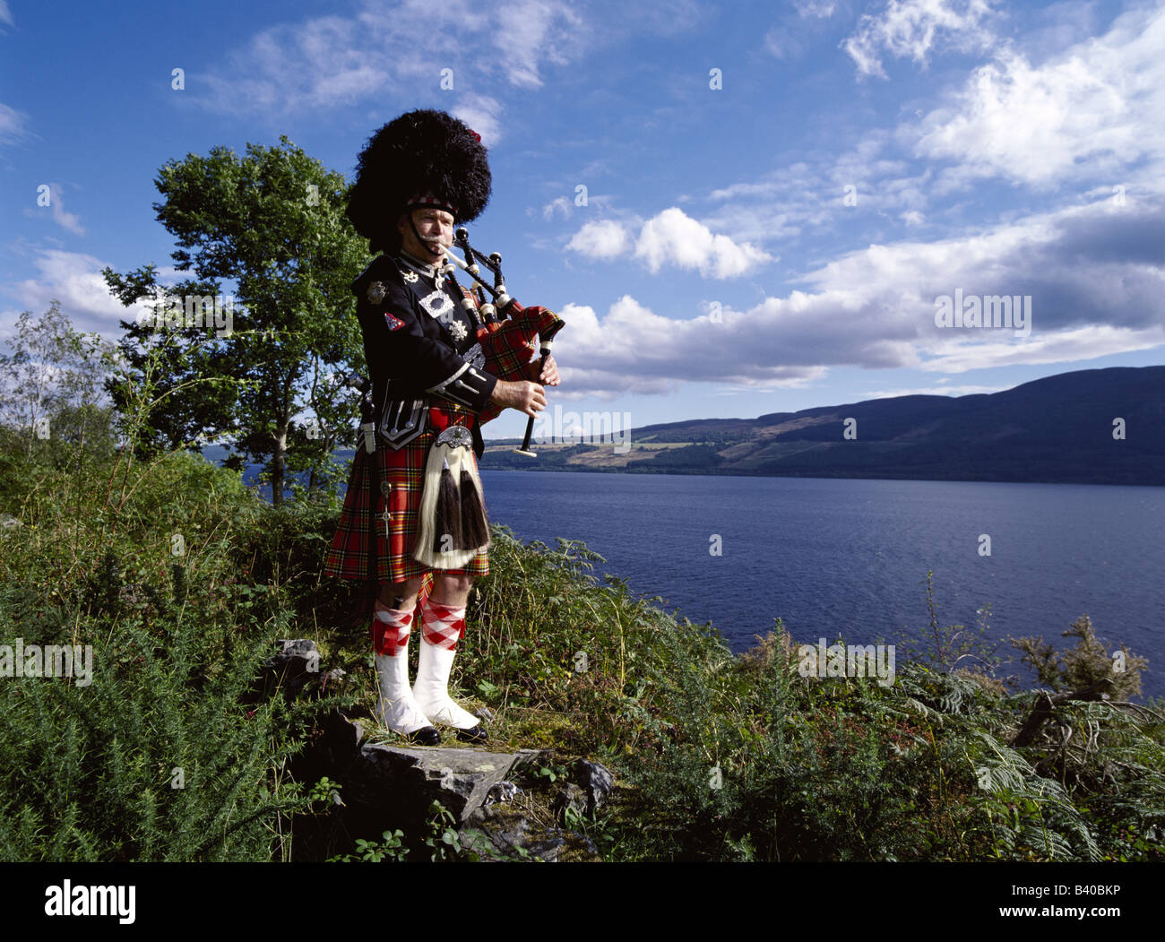 dh LOCH NESS ECOSSE Scottish Piper cornemuses tartan kilt uniforme Piping cornemuse cornemuse dans les hautes terres traditionnel highland sac tuyaux homme hommes Banque D'Images