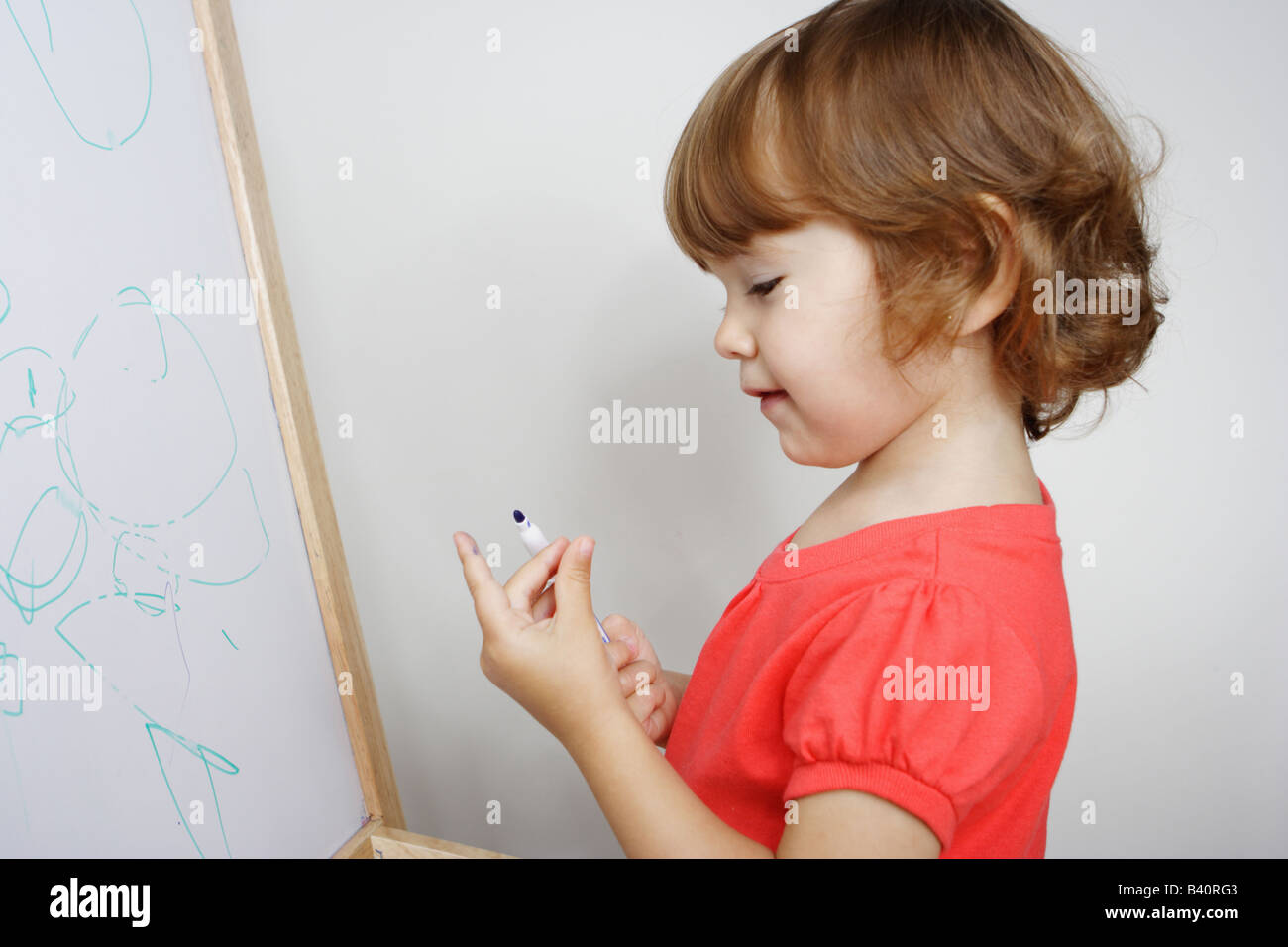 Deux ans d'un bébé fille de peindre sur un tableau blanc est à la recherche à son doigt sale sourire. Banque D'Images