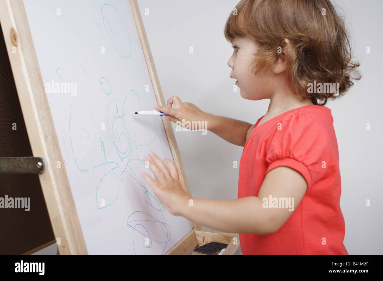 A deux ans bébé fille s'appuie sur un tableau blanc tenant maladroitement  d'un feutre Photo Stock - Alamy