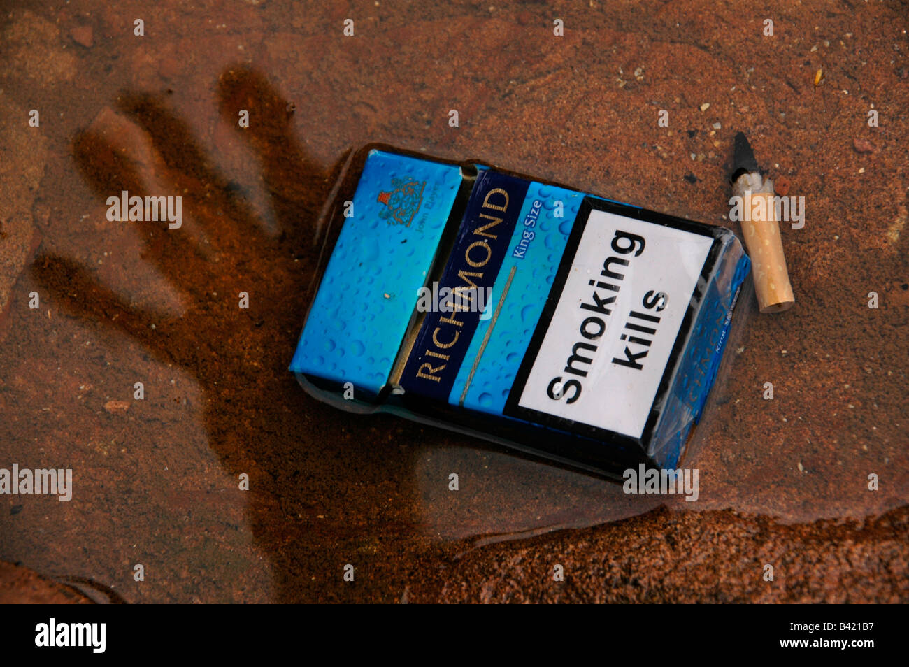 Une boîte vide de cigarettes et un demi-mensonge dans l'eau peu profonde avec l'ombre d'une main tendre la main. Banque D'Images