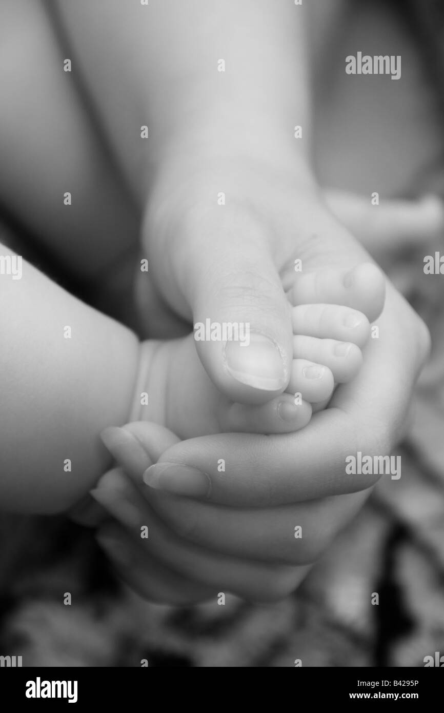 Close-up of a mother holding her baby's foot dans sa main, image monochrome. Banque D'Images