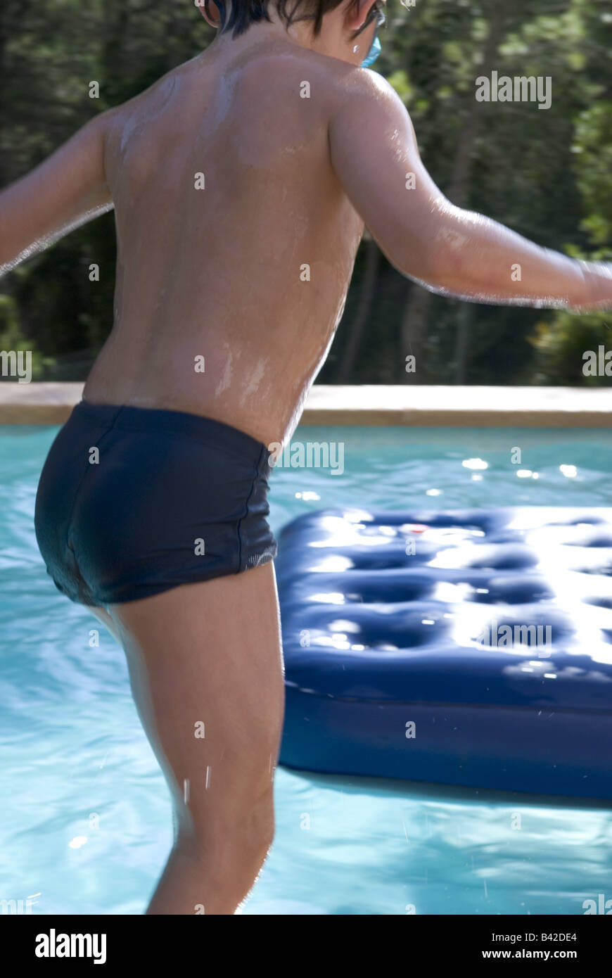 Détail de l'arrière du jeune garçon sur le point de sauter dans une piscine sur lilo en attente Banque D'Images