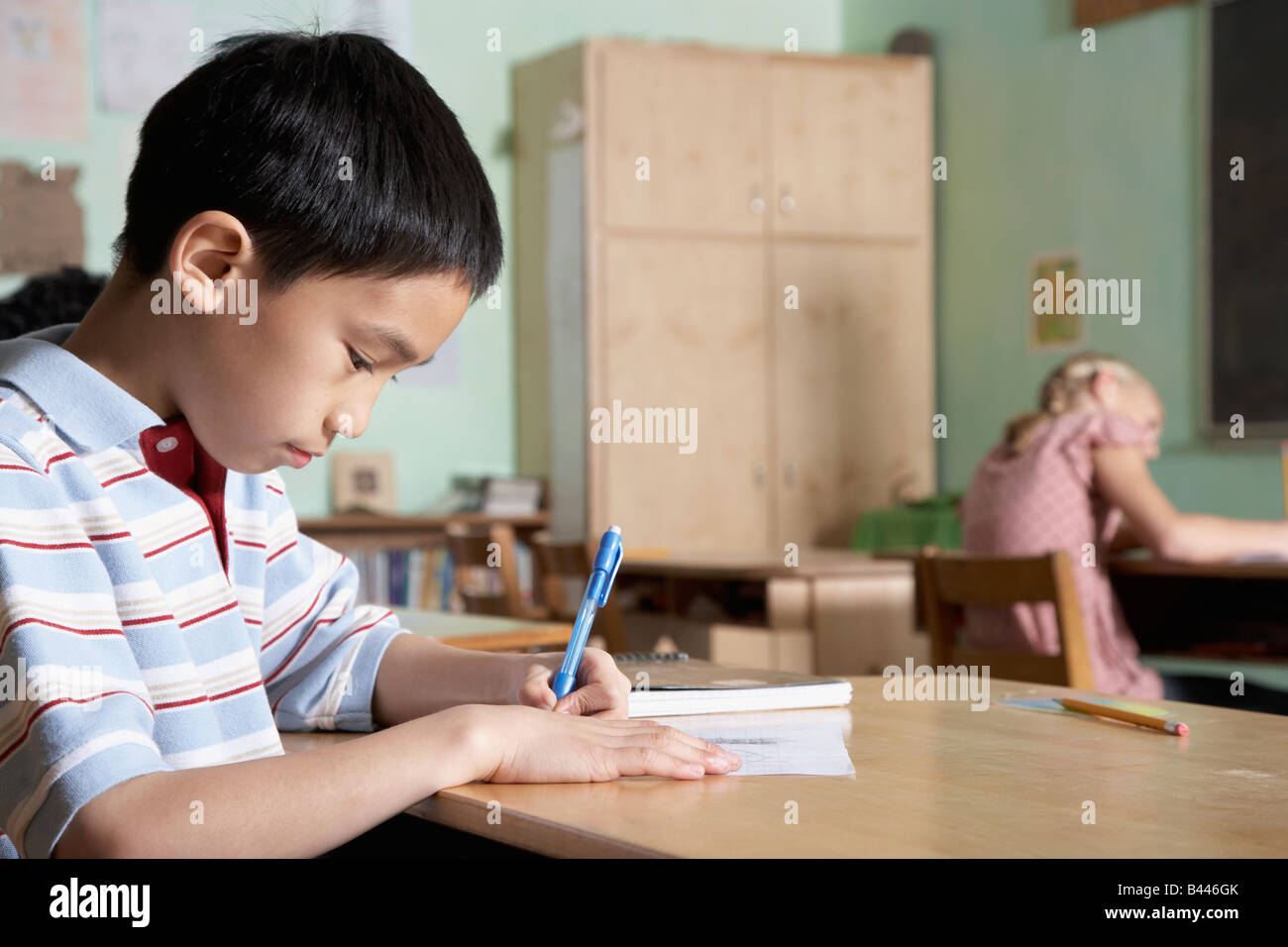 Asian boy writing in classroom Banque D'Images