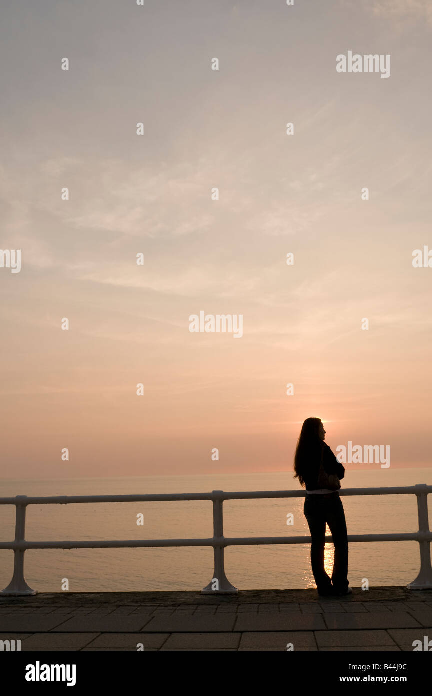 Jeune femme seul découpé sur le coucher de soleil sur la promenade de l'ouest du pays de Galles Aberystwyth UK Banque D'Images