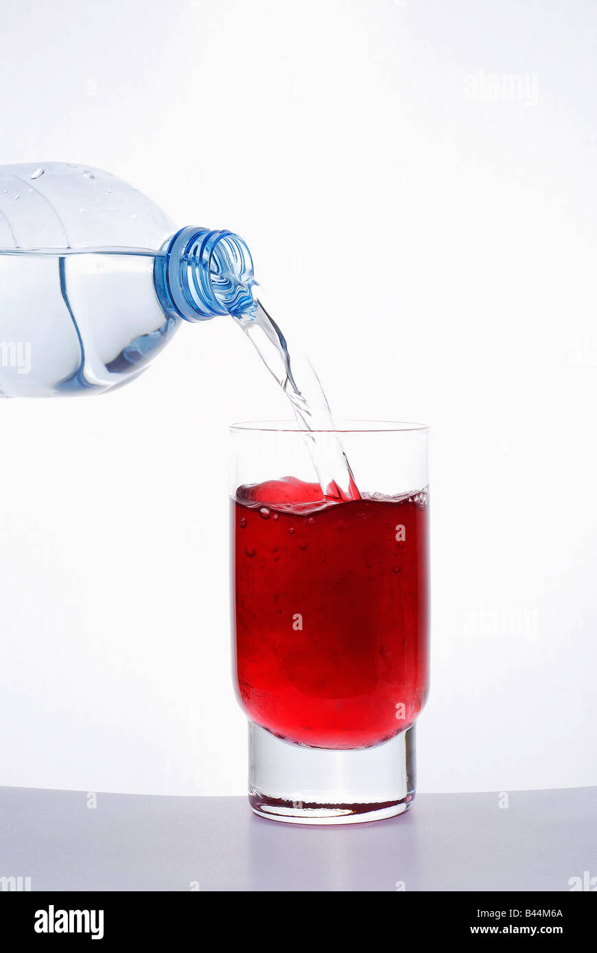 Verser de l'eau dans un verre de sirop de grenadine Photo Stock - Alamy