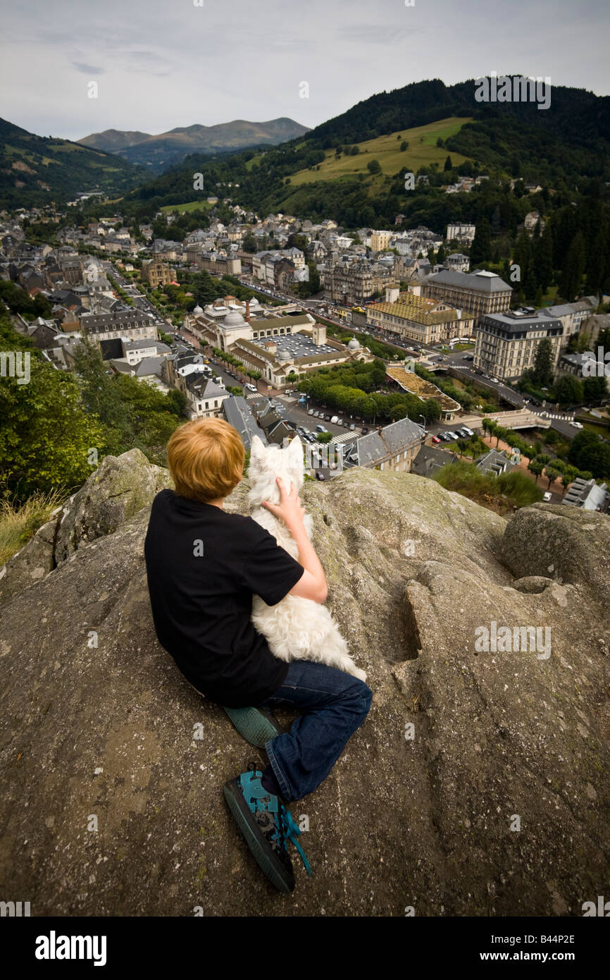 Un jeune garçon regardant La Bourboule ville avec son chien. Jeune garçon contemplant avec son chien la ville de La Bourboule. Banque D'Images