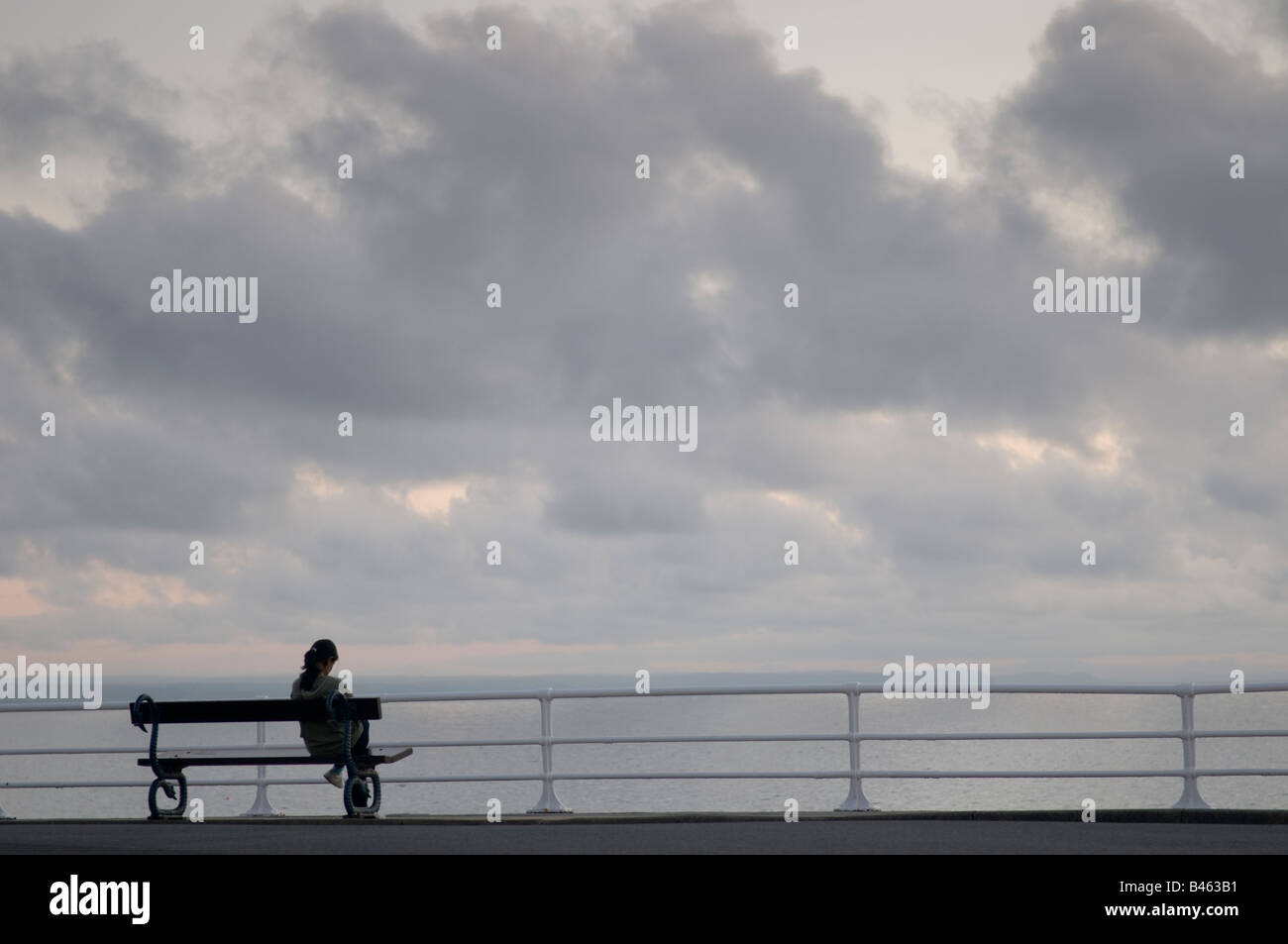 Jeune femme assis sur un banc seul sur Aberystwyth, promenade en début de soirée Banque D'Images