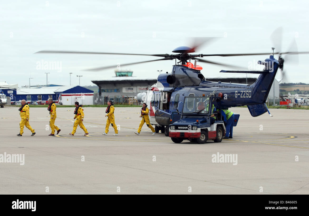 Les travailleurs du pétrole de la mer du Nord au large des côtes dans des combinaisons de survie de descendre un hélicoptère superpuma Bristow à l'aéroport d'Aberdeen, Écosse, Royaume-Uni Banque D'Images