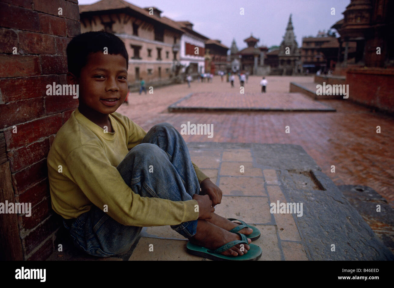Young Nepali garçon assis sur les immeubles de la chaussée à Katmandou Népal Bhaktapur distance Banque D'Images
