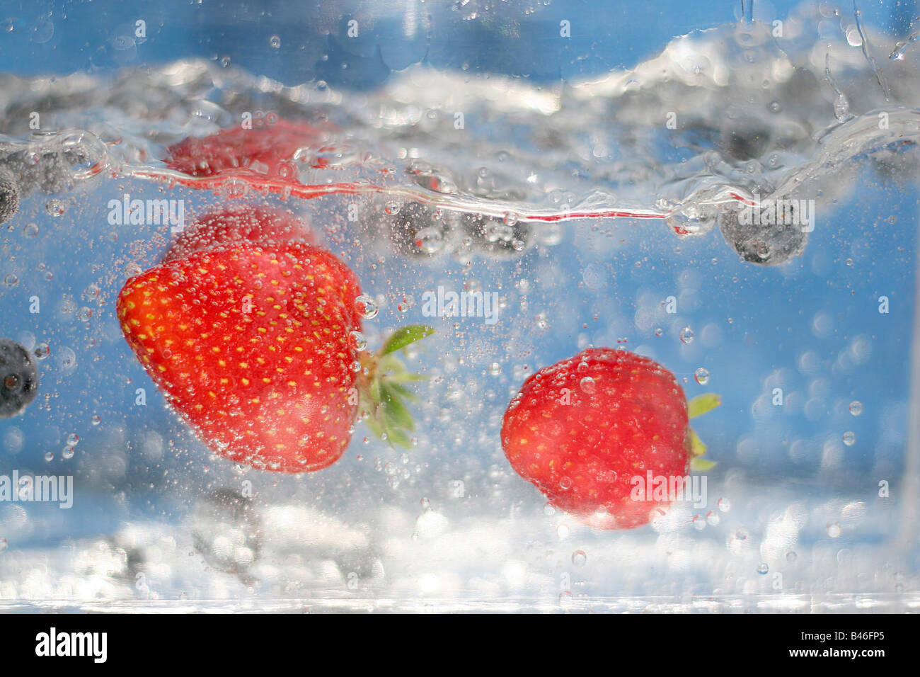 Quelques fraises rouges juteux plongeant dans l'eau claire Banque D'Images