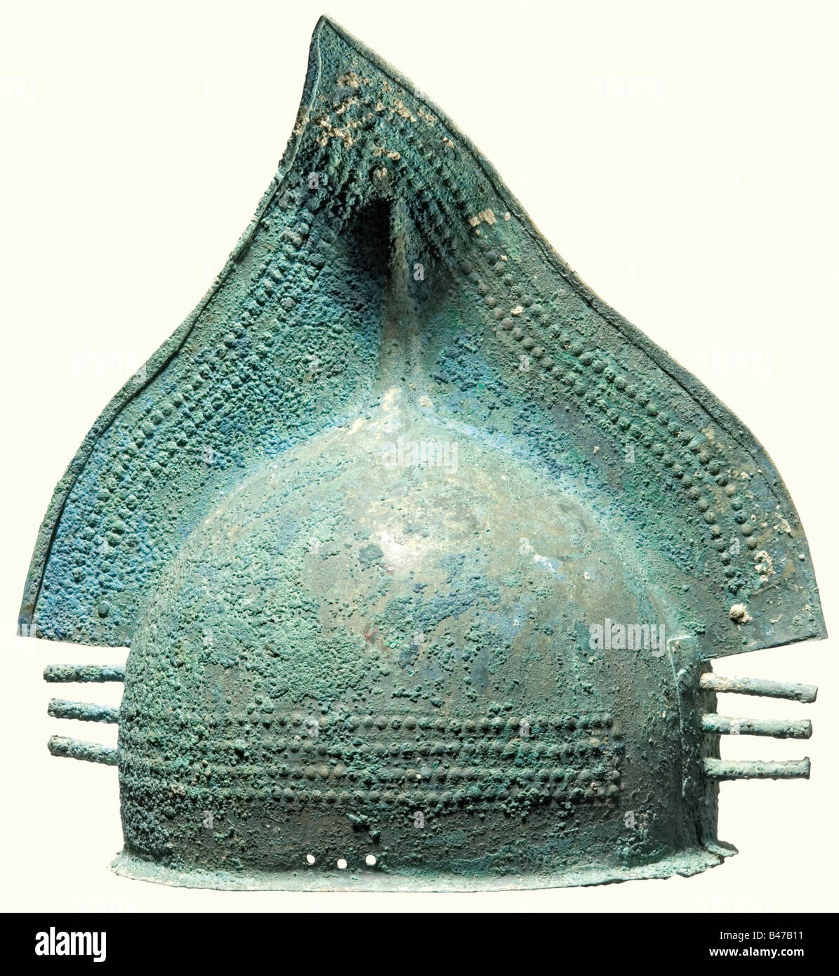 Un casque à peigne en bronze, âge du début du fer, IXe et 8ème siècle avant J.-C. UN casque en bronze fait de deux plaques avec une bordure inférieure étroite et en protuding. Le point du grand sabot triangulaire est légèrement tordu. Les deux moitiés du casque sont fixées ensemble par des bords tournés sous les bords ou un rivetage. Les côtés avant et arrière du casque se chevauchent et sont rivetés avec de lourdes plaques de bronze, chacune décorée d'un cercle et chacune avec trois pointes saillantes en forme de barre. Le corps du casque et le sabot sont décorés de grands et petits boutons. De chaque côté se trouvent trois trous pour fixer la jugulaire. Greeni, Banque D'Images