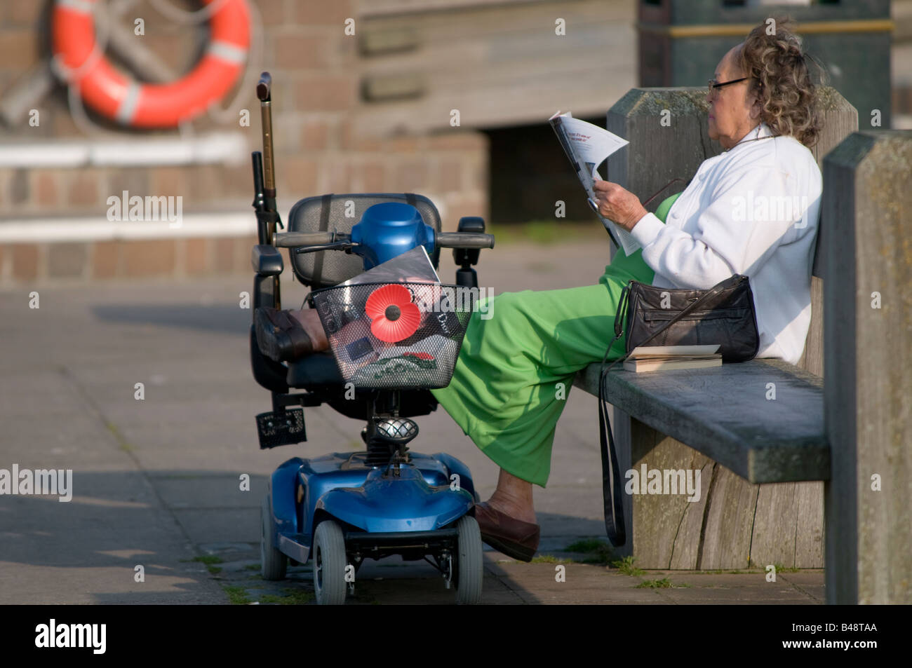 Femme avec scooter de mobilité reading newspaper in the sunshine Aberaeron Ceredigion Pays de Galles UK Banque D'Images