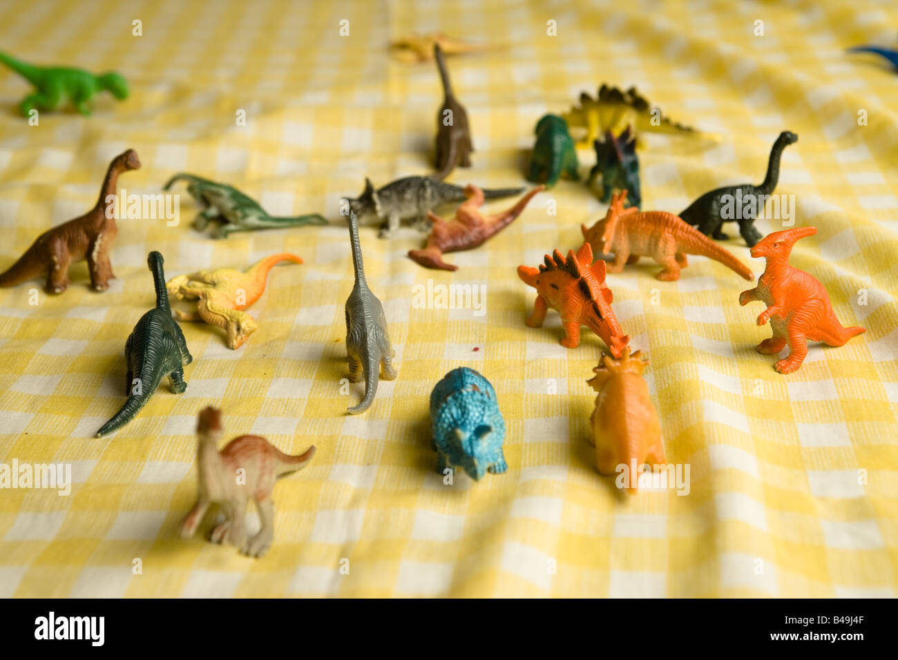 Bouquet coloré de dinosaures jouets en plastique bon marché debout sur un tissu blanc et jaune à carreaux avant une bataille de titans Banque D'Images