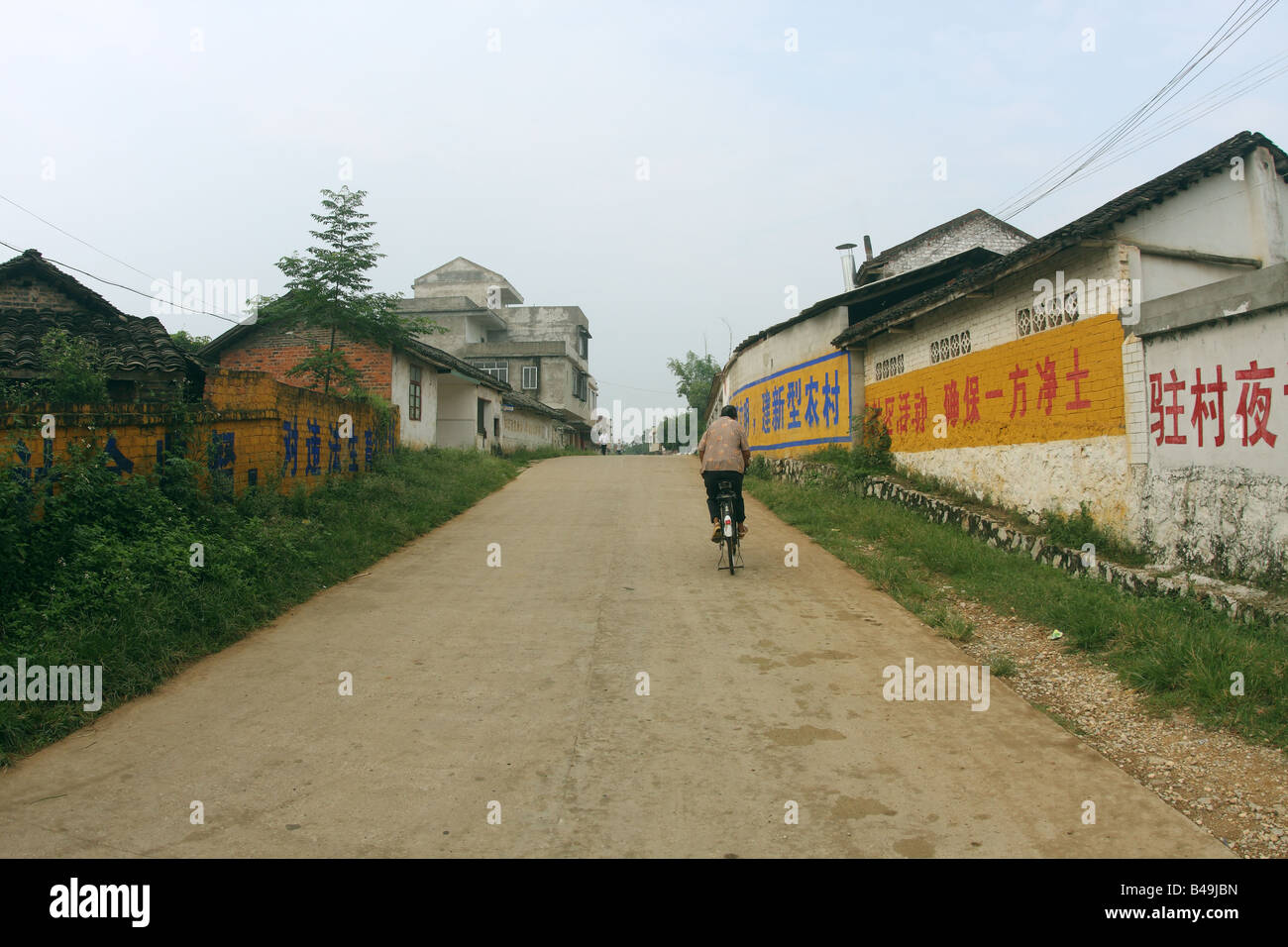 Woman riding bicycle paysan seul la poussière dans la rue sud-ouest rural village chinois, passé de la propagande chinoise perspective Banque D'Images