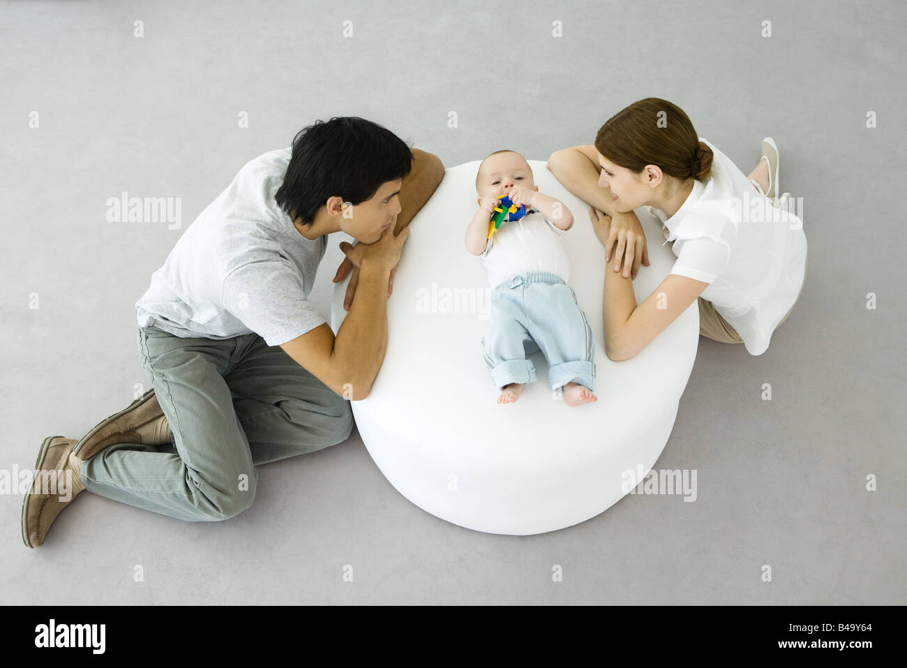Les jeunes parents appuyé contre un pouf, regardant bébé couché entre eux Banque D'Images