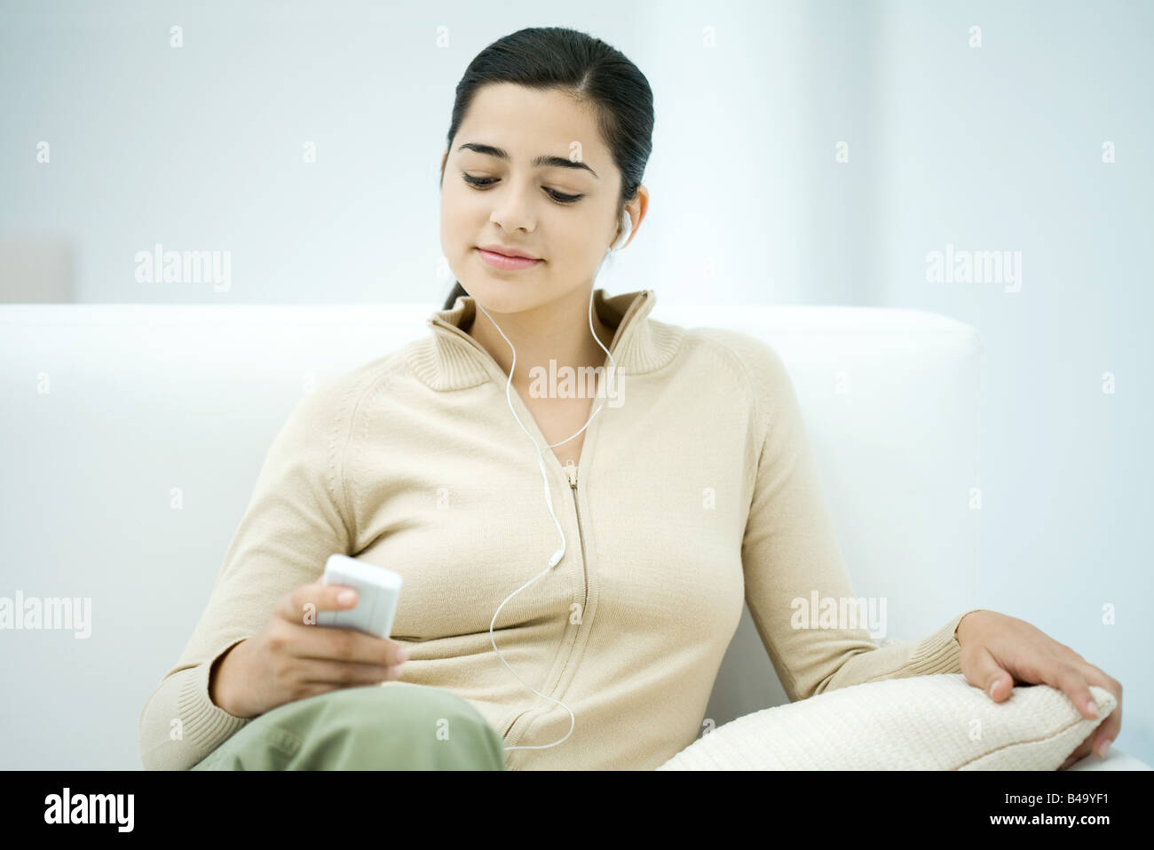 Jeune femme assise sur un canapé, listening to MP3 player Banque D'Images
