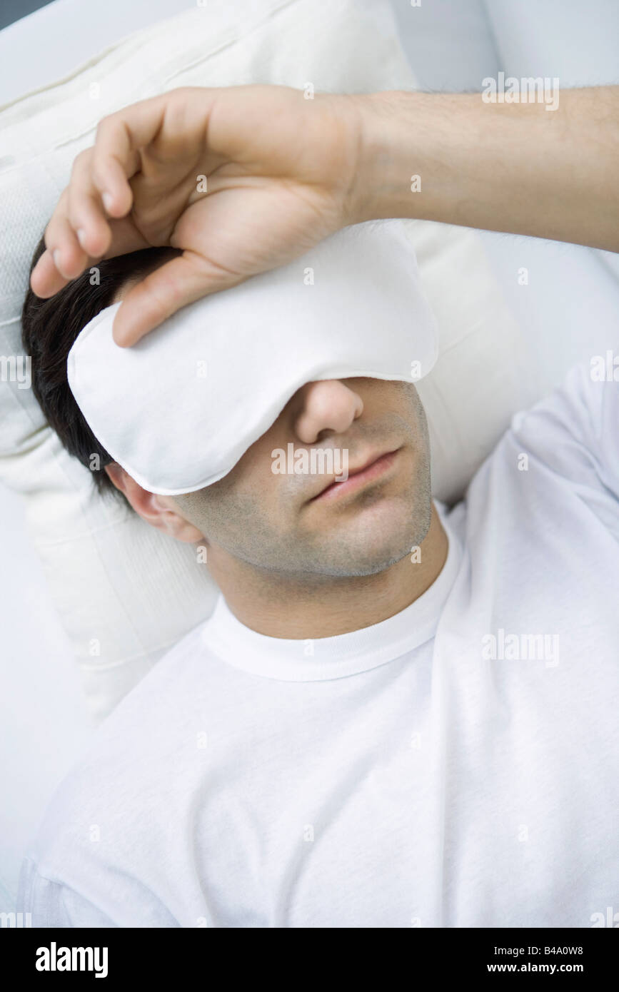 Homme couché avec un masque pour les yeux, la main sur la tête Banque D'Images