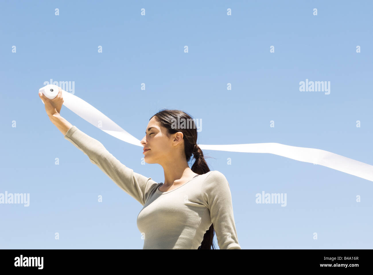Woman holding up rouleau de papier à l'extérieur, les yeux clos, low angle view Banque D'Images