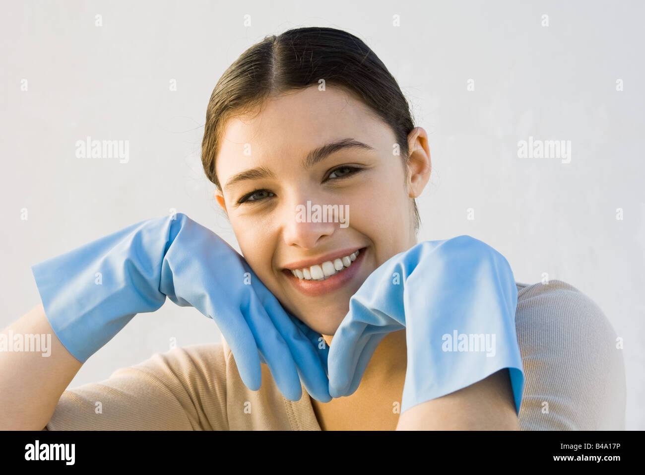 Jeune femme portant des gants de caoutchouc, smiling at camera, les mains sous le menton Banque D'Images