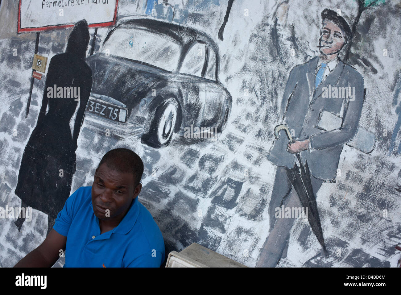 Un homme d'ascendance créole détend la fin de l'après-midi devant une murale montrant une scène de la vie parisienne à l'époque coloniale Kourou Banque D'Images