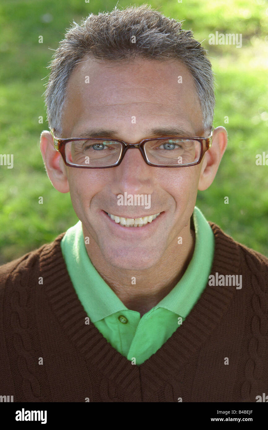 Head and shoulders Portrait d'un homme aux cheveux gris portant des lunettes cerclées de corne une chemise de golf vert et un pull marron col en V Banque D'Images