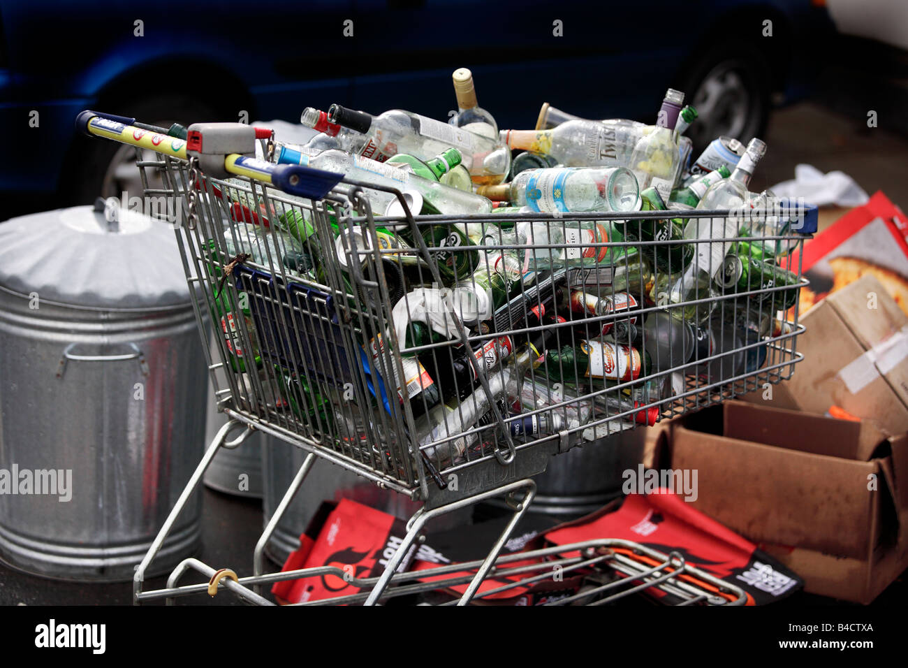 Un chariot de supermarché plein de bouteilles et canettes de boissons vides en attente de collection sur le trottoir devant une télévision à Birmingham. Banque D'Images