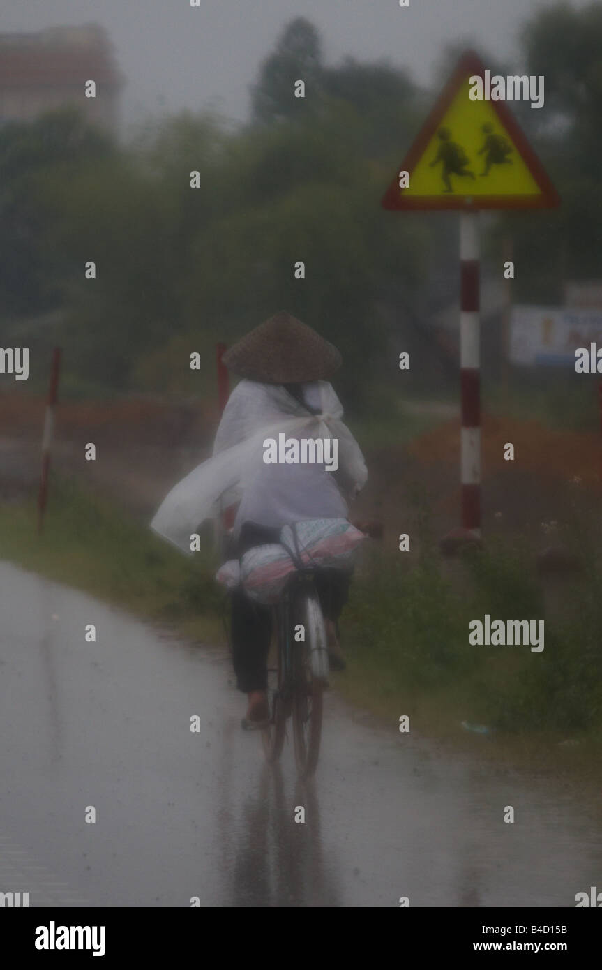 Une vietnamienne équitation le vélo sous la pluie Banque D'Images