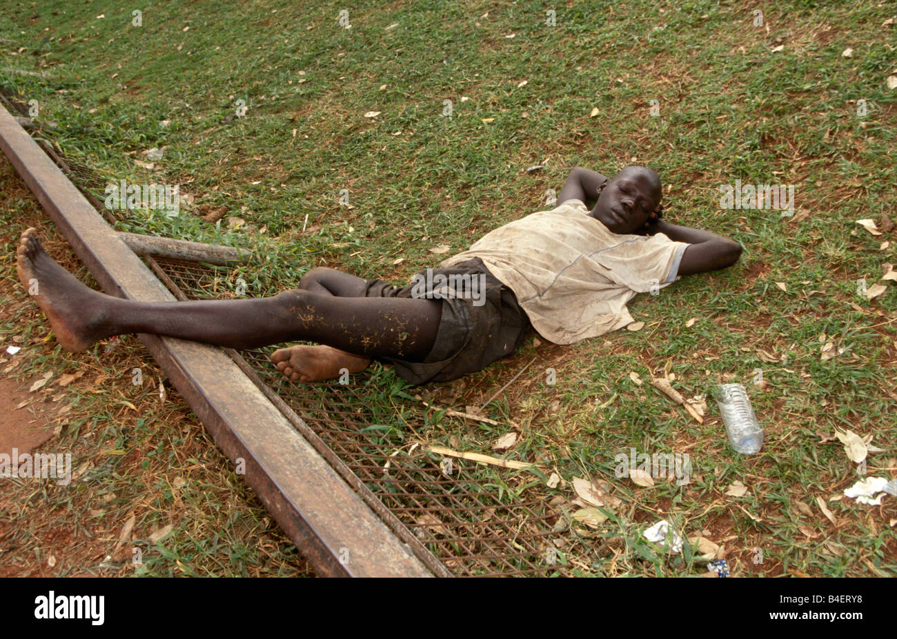 Garçon sans-abri étendit sur le sol, dormant sur les effets de l'inhalation de vapeurs de colle. Kampala, Ouganda. Banque D'Images