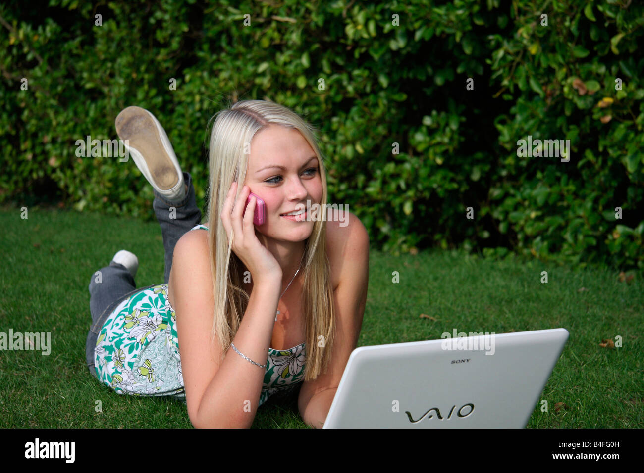 Girl lying on grass avec téléphone mobile et un ordinateur portable Banque D'Images