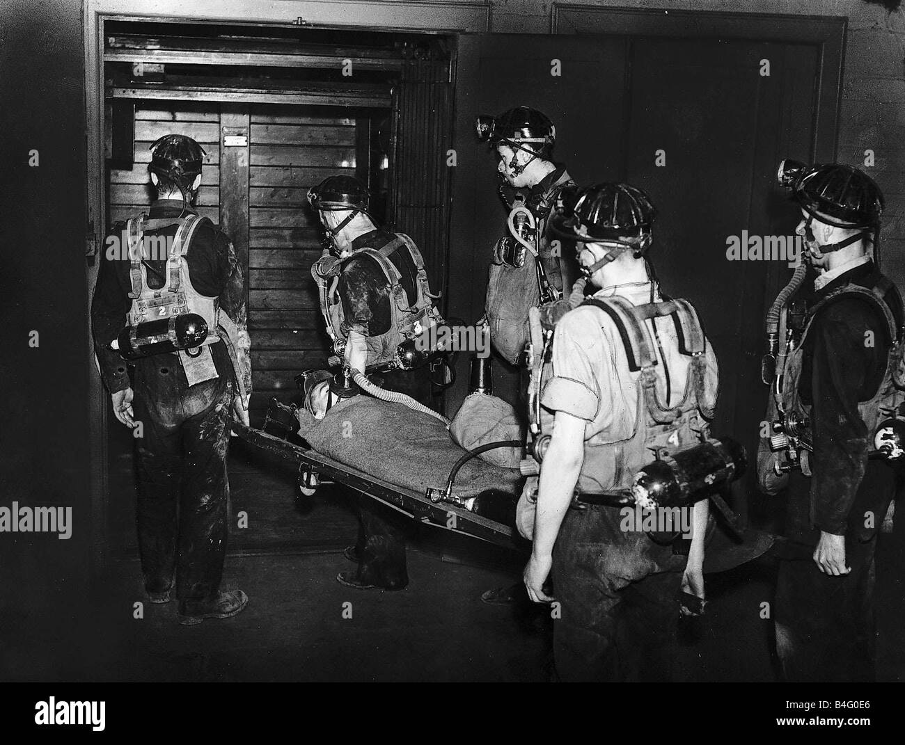 Services de sauvetage minier transporter un mineur portant un masque à oxygène sur une civière dans une cage à ciel ouvert après avoir ramassé une blessure vers 1965 Banque D'Images