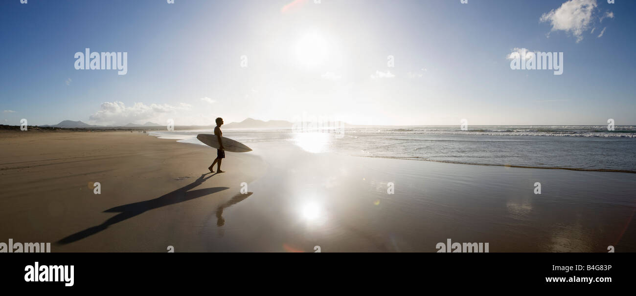 Un jeune homme debout sur une plage, et l'exécution un surf Banque D'Images
