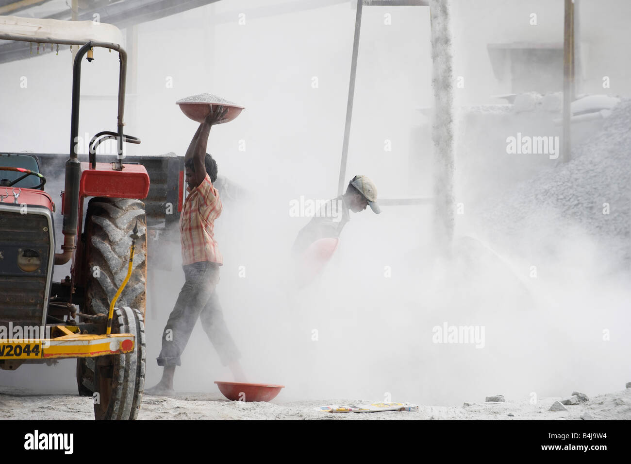 Les hommes indiens de mettre de la pierre concassée dans une remorque, entouré par la poussière, sans protection, à l'écrasement fonctionne. L'Andhra Pradesh. L'Inde Banque D'Images