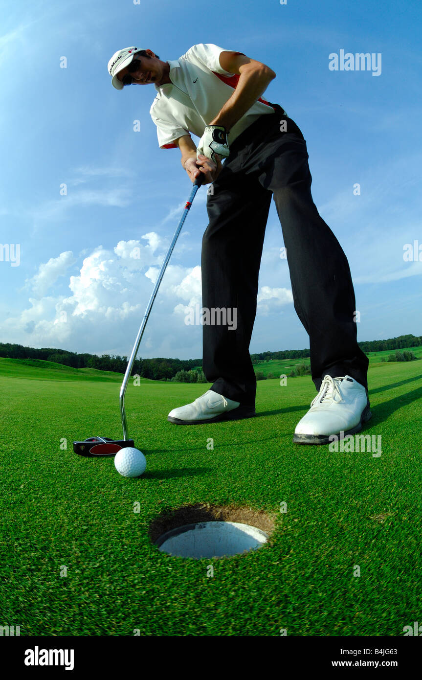 Une large vue vers le bas et la conduite d'un joueur de golf mettre près du trou sur le green de golf - France Banque D'Images