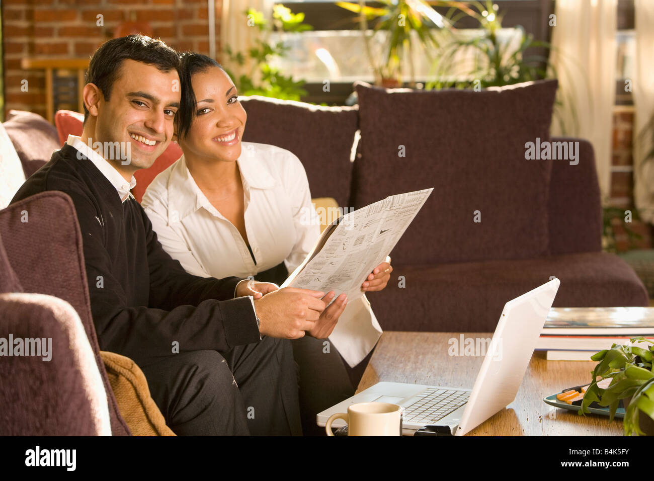 Mixed Race woman reading newspaper in living room Banque D'Images