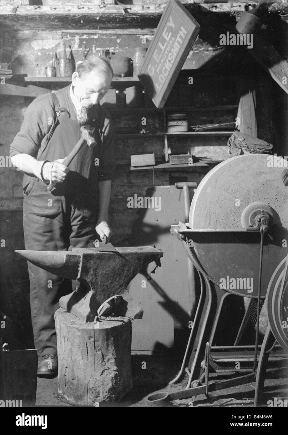 Un forgeron travaille dans sa forge l'élaboration d'une feuille de métal sur son enclume, vers 1940 Banque D'Images