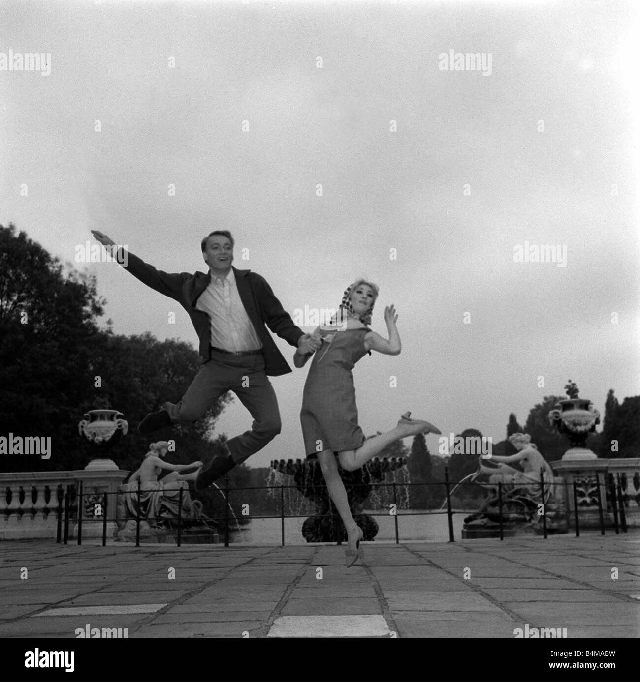 Frank Ifield singer avec l'actrice Annette Andre Juin 1965 sauter en l'air la main dans la main dans les jardins de Kensington Banque D'Images