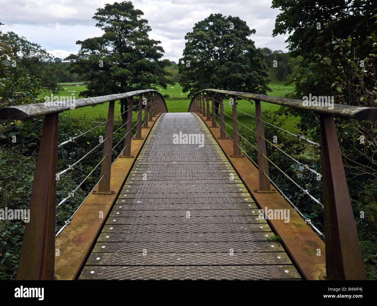 Vue sur métal rouillé pont menant dans les champs ouverts dans la campagne boisée dans le Nord de l'Angleterre Cumbria Banque D'Images