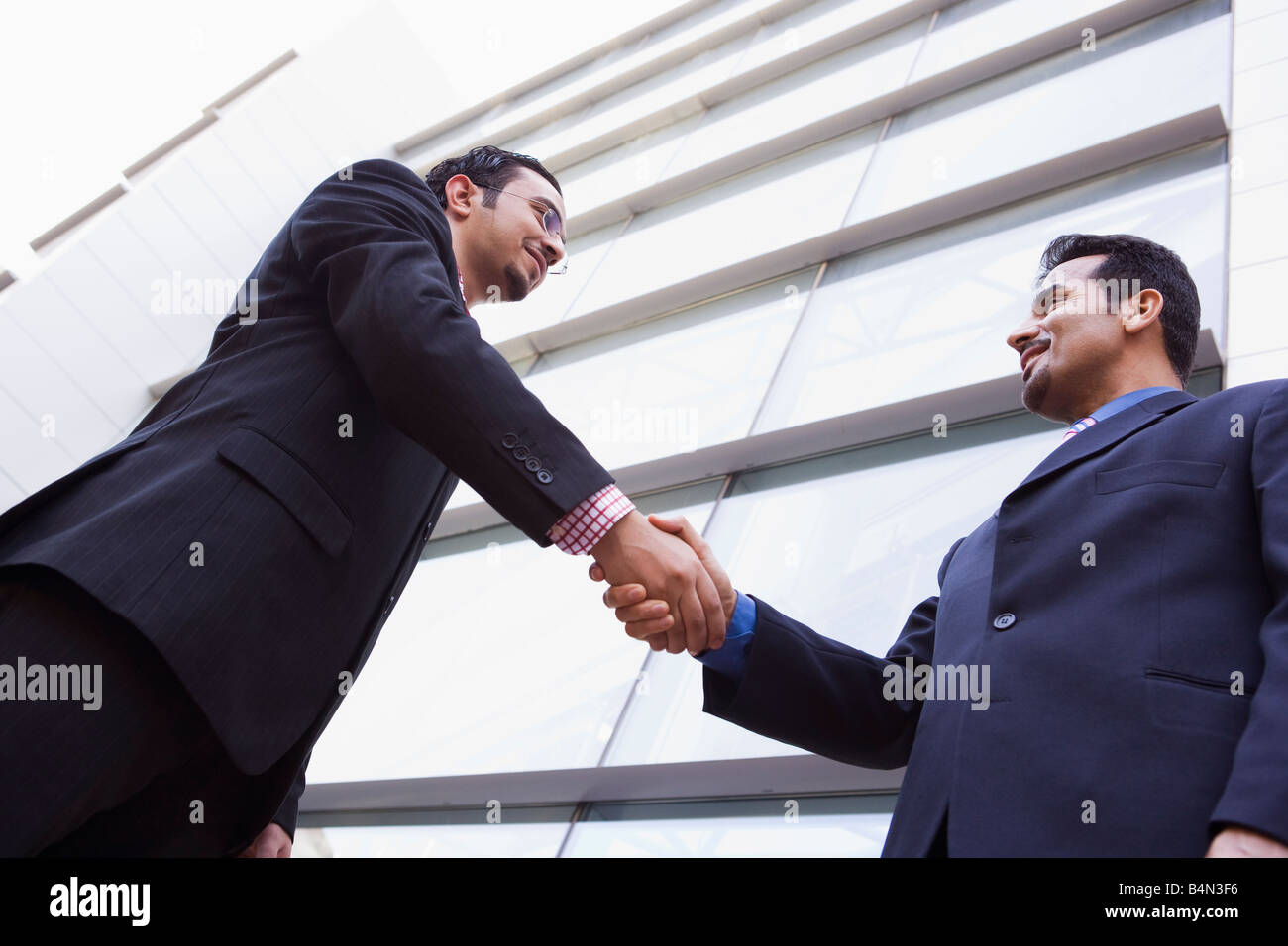Deux hommes d'affaires à l'extérieur par la construction d'une poignée de main et sourire (high key/focus sélectif) Banque D'Images