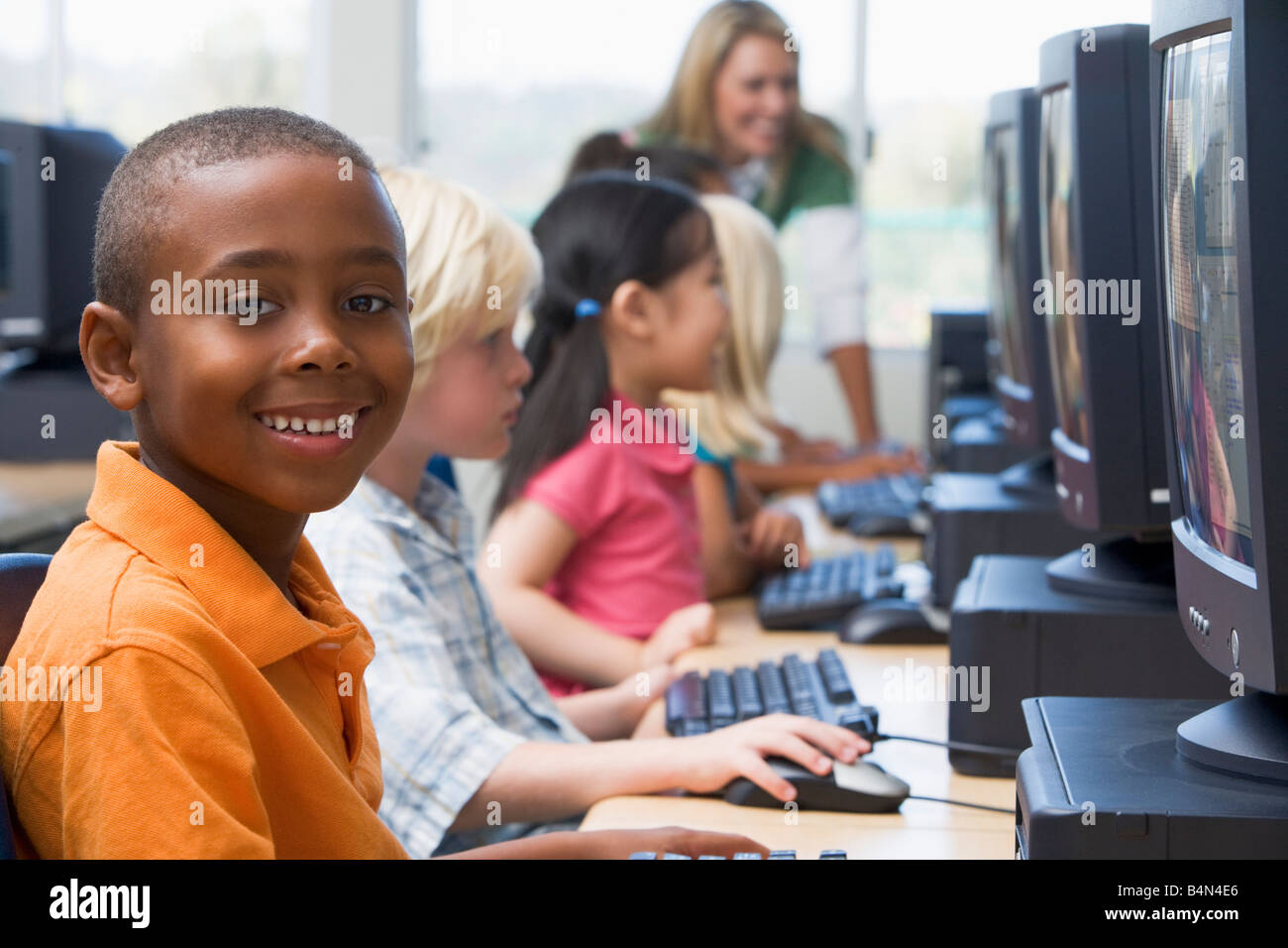 Les enfants devant un ordinateur avec l'enseignant en arrière-plan (profondeur de champ/high key) Banque D'Images