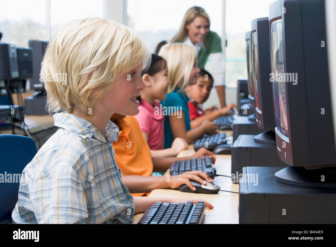 Les enfants devant un ordinateur avec l'enseignant en arrière-plan (profondeur de champ/high key) Banque D'Images